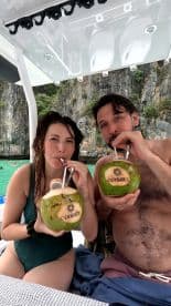 A couple enjoys refreshing coconut cocktails aboard a boat, capturing the essence of a fun and relaxing day on the water with the stunning backdrop of nature.