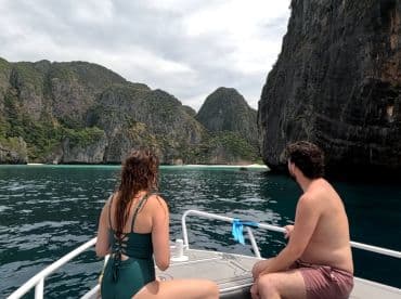 A couple enjoys a scenic boat ride, taking in the breathtaking views of lush cliffs and a secluded beach — perfect for adventure seekers exploring hidden gems.