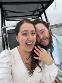 A joyful couple celebrates their engagement aboard a boat, showcasing the beautiful ring and their happiness — a perfect moment for romantic adventures on the water.