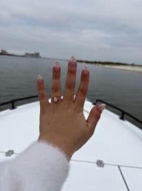 A hand displaying a beautiful engagement ring while on a boat, capturing a moment of celebration on the water.
