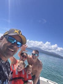 A joyful family poses for a selfie on a boat, showcasing their fun day out on the water with life jackets and smiles all around.