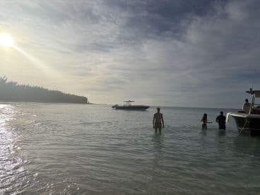 A group of friends enjoys a relaxing day at the beach, wading in the shallow waters with a boat anchored nearby — a perfect setting for summer fun and adventure.