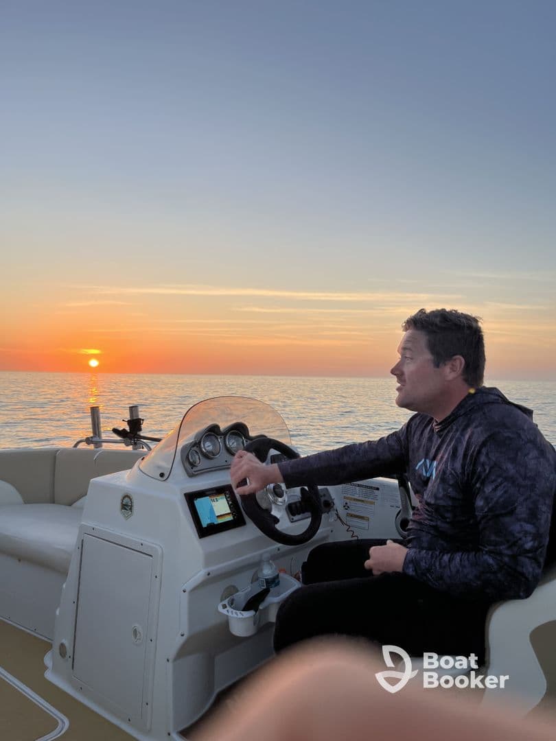 A man navigates a boat at sunset, creating a serene atmosphere perfect for evening cruises. The stunning sunset reflects on the water, enhancing the boating experience.