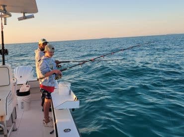 A joyful moment as a child and an adult fish together at sunset, creating lasting memories on the open water.
