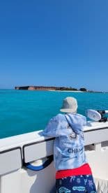 A child gazes at a historic island fort from the deck of a boat, surrounded by stunning turquoise waters — a perfect moment of exploration on the water.