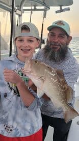 A joyful moment captured as a child proudly holds up a freshly caught fish with an adult on a fishing trip — a perfect family bonding experience on the water.