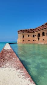 A scenic view of a historic structure by the water, showcasing the beauty of the surrounding turquoise sea.