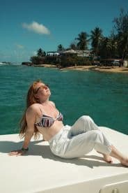 A woman relaxes on the deck of a boat, soaking up the sun with a stunning ocean backdrop — perfect for a day of leisure on the water.