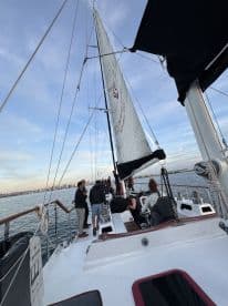 A lively group enjoys a sailing experience on a yacht, with a stunning city skyline in the background — perfect for social gatherings and scenic adventures on the water.