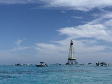 A vibrant scene featuring multiple boats near a historic lighthouse, showcasing the beauty of a coastal day on the water.