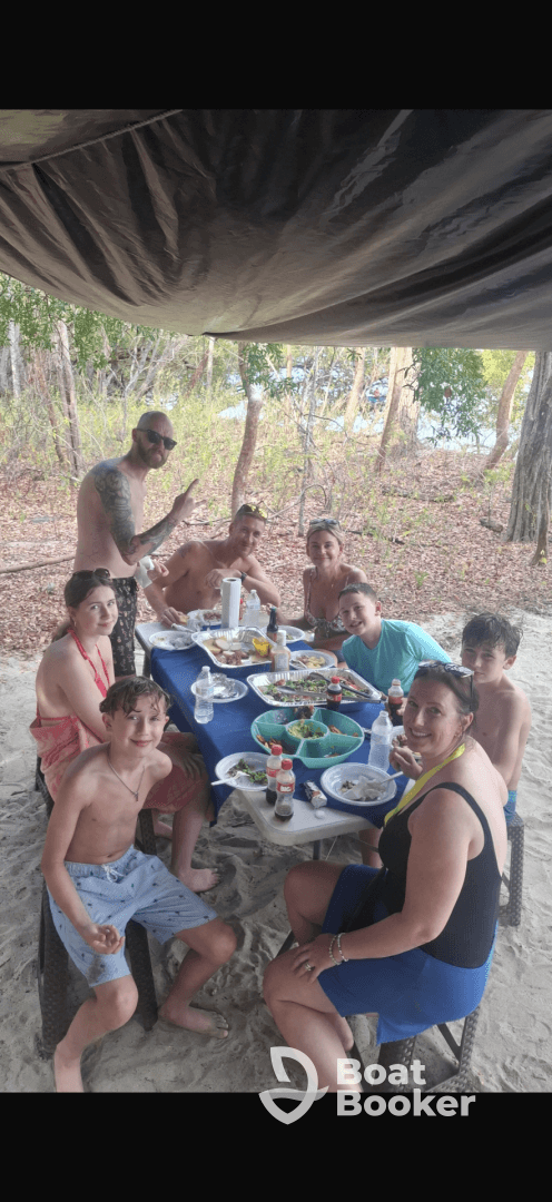 A joyful group enjoys a meal together on the beach, surrounded by nature — perfect for family gatherings and celebrations.