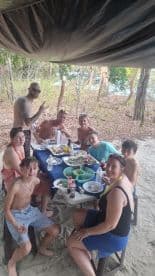 A joyful group enjoys a meal together on the beach, surrounded by nature — perfect for family gatherings and celebrations in a tropical setting.