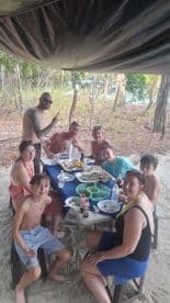 A joyful group enjoys a meal together under a canopy on the beach, perfect for family gatherings and celebrations while soaking up the sun.