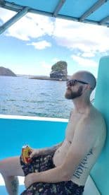 A man enjoys a refreshing drink while relaxing on a boat, with stunning island scenery in the background — perfect for a day of leisure on the water.