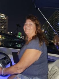 A woman enjoys a night ride on a boat, illuminated by city lights in the background — a perfect setting for evening cruises.