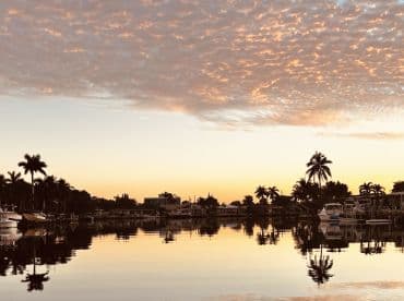 A serene sunset view over a calm waterway, reflecting the vibrant colors of the sky and surrounding palm trees — a picturesque moment perfect for relaxation and scenic boat trips.