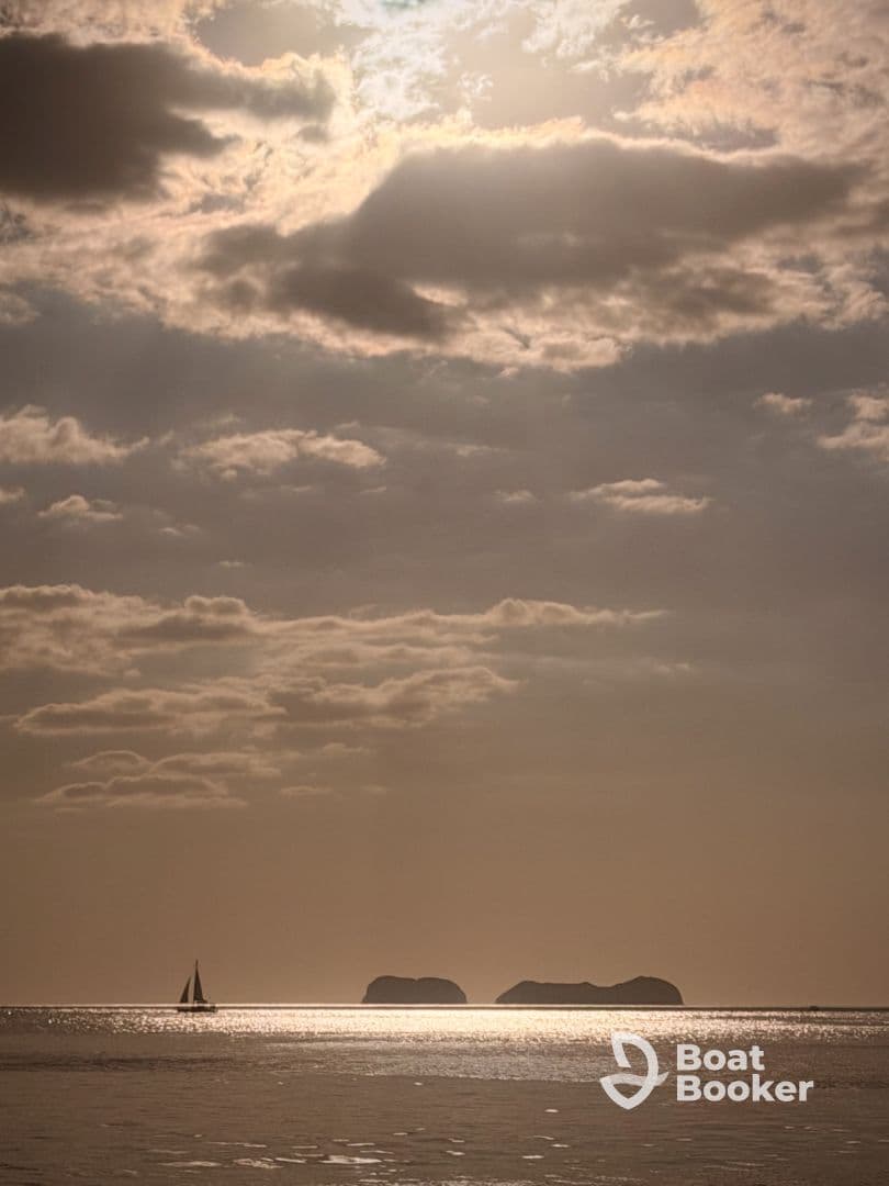 A serene sunset view featuring a sailboat gliding across the shimmering water, with distant islands creating a picturesque backdrop.