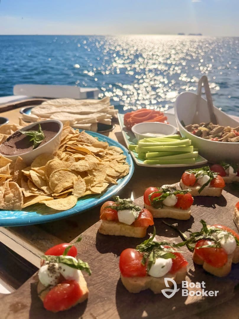 A beautifully arranged spread of snacks including bruschetta, chips, and fresh vegetables, perfect for enjoying on a boat trip while taking in the scenic ocean views.