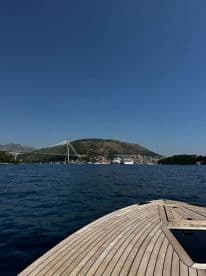 A stunning view of a boat's bow cutting through the clear waters, with a picturesque backdrop of a bridge and hillside town, perfect for showcasing scenic boating adventures.