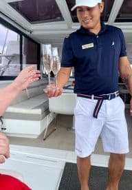 A server presents two glasses of champagne to a guest aboard a luxurious boat, showcasing the high-end service and amenities available for a memorable experience.