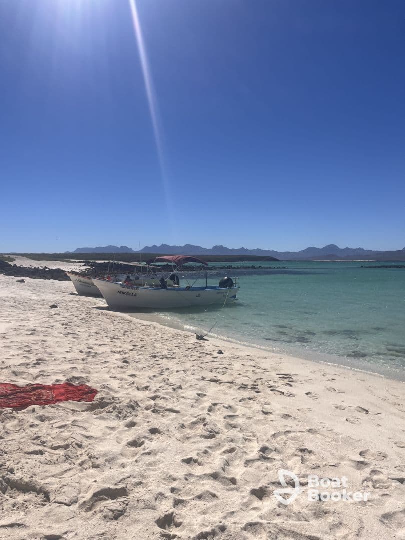 Two boats are docked on a pristine beach with clear blue skies and distant mountains, perfect for a day of relaxation and exploration.