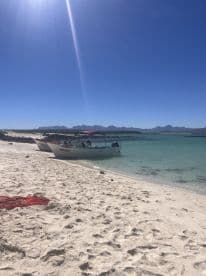 Two boats are docked on a pristine beach with clear blue skies and distant mountains, perfect for a day of relaxation and exploration.