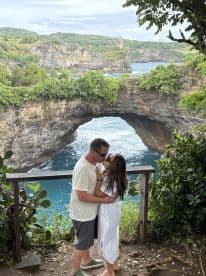 A romantic moment between a couple at a scenic viewpoint, framed by lush greenery and a stunning coastal arch — perfect for capturing love amidst nature's beauty.