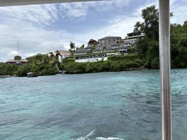 A scenic view of a lush coastline with charming buildings nestled among greenery, showcasing the beauty of the area from the water.