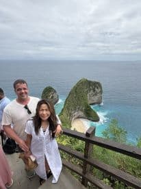 A couple poses for a photo with stunning coastal rock formations in the background, capturing a memorable moment at a beautiful beach destination.