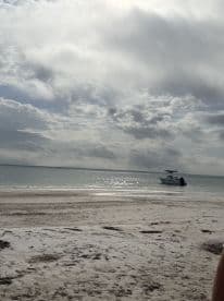 A serene view of a boat anchored near the beach, with cloudy skies reflecting on the water — an ideal setting for a relaxing day by the shore.