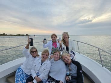 A joyful group of friends raises their drinks in celebration aboard a boat during a picturesque sunset cruise, perfect for memorable gatherings on the water.