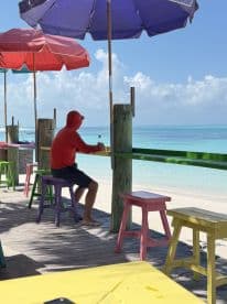 A person enjoys a refreshing drink while seated under colorful umbrellas at a beachside bar, capturing the essence of relaxation in a tropical paradise.
