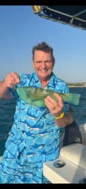 A joyful fisherman proudly displays his catch aboard a boat, capturing the excitement of a successful fishing trip.