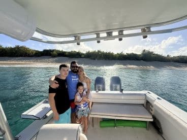 A joyful family poses together on their boat with a beautiful beach backdrop, capturing a memorable moment during their day on the water.