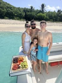 A joyful family poses on a boat with a delicious spread of snacks, enjoying a sunny day at the beach — perfect for memorable family outings.