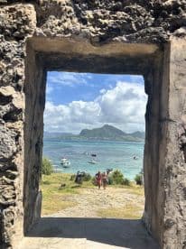 A couple strolls along the beach with a stunning view of boats and a mountainous island in the background, capturing the essence of a perfect day on the water.