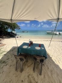 A beachside dining setup featuring a table with plates and drinks, perfect for enjoying meals with a stunning ocean view.
