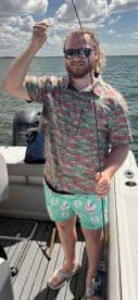 A man proudly displays his catch while fishing on a boat, showcasing the excitement of a successful day on the water.