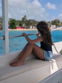 A young girl enjoys the serene ocean view while sitting on the deck of a boat, capturing a moment of relaxation and tranquility on the water.