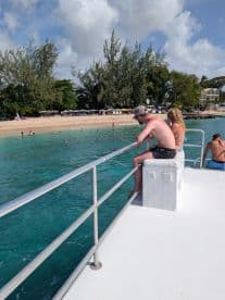 A couple enjoys a relaxing moment on the deck of a pontoon boat, casting lines into the clear waters while a beautiful beach scene unfolds in the background.