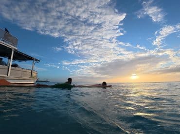 A couple enjoys a serene sunset while floating in the water next to a pontoon boat, creating a perfect romantic getaway on the water.
