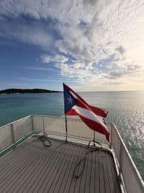 A stunning view from the deck of a boat featuring the Puerto Rican flag, set against a backdrop of calm waters and a picturesque sky — perfect for showcasing maritime pride.