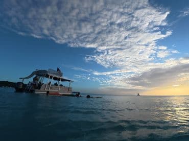 A picturesque scene of a boat at sunset with guests enjoying the water, capturing the essence of a perfect day on the ocean.