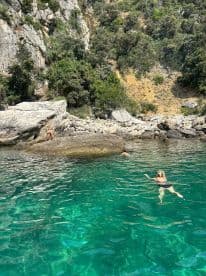 Two individuals enjoy a refreshing swim in crystal-clear waters near a rocky coastline, perfect for beach adventures and exploration.