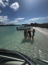 A group of friends enjoys a fun day at the beach, posing in shallow water with a boat anchored nearby — perfect for memorable summer outings.