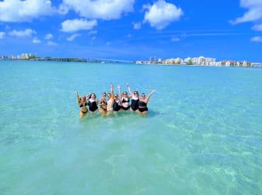 A joyful group of friends celebrates in the shallow waters, enjoying a fun day at the beach — perfect for summer outings and group adventures.