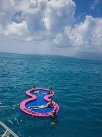 A group of friends enjoys a sunny day on a floating mat in the turquoise waters, perfect for relaxation and fun in the sun.