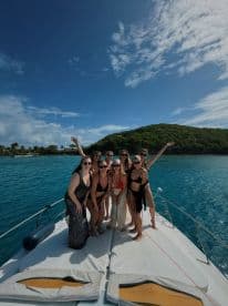 A joyful group of friends poses on the bow of a boat, celebrating under the sun — perfect for unforgettable outings and adventures on the water.