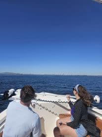A couple enjoys a scenic boat ride with a stunning city skyline in the background, perfect for a day of adventure on the water.