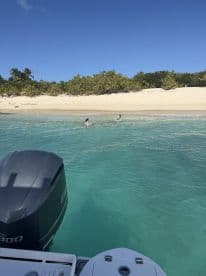 Two individuals enjoy a refreshing swim in the clear turquoise waters near a sandy beach, capturing the essence of a perfect day on the water.